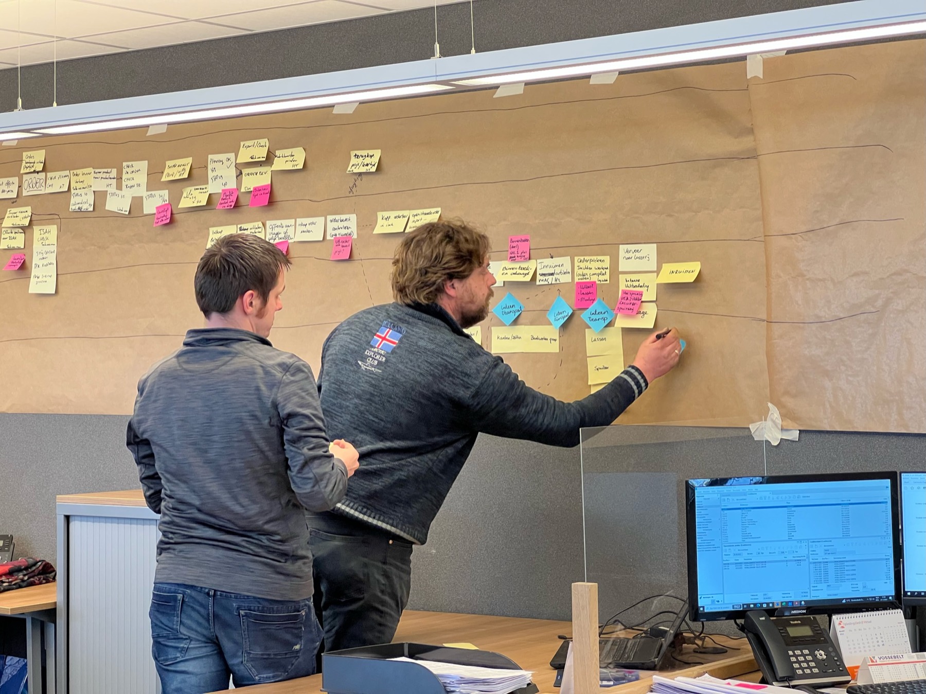 Consultant van PowerOne wijst naar een BPMN-diagram op een grote print aan de muur.