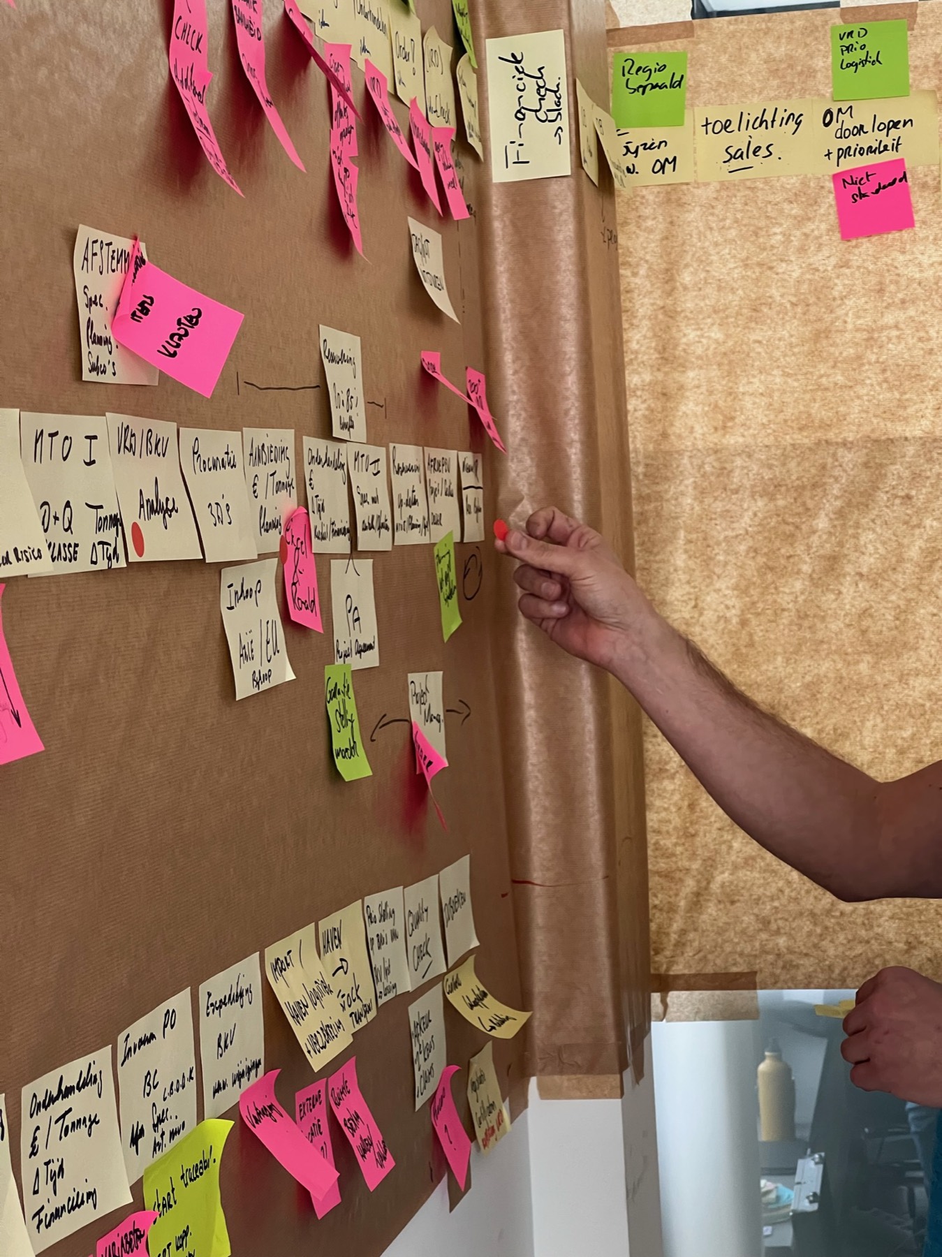Consultant wijst een collega op een geprioriteerde actie op de post-it-muur.