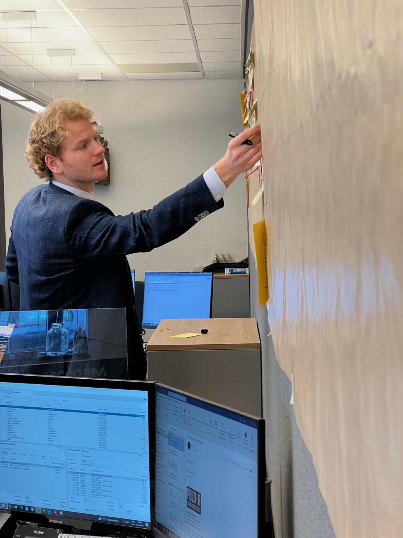 Close-up van een procesmuur vol post-its, met een hand die een knelpunt markeert.