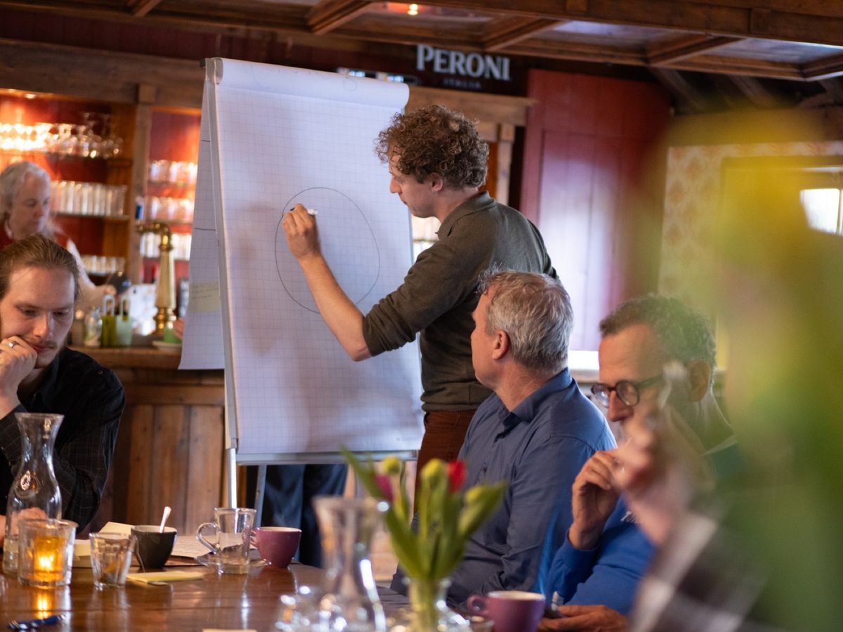 Christiaan Strikwerda tekent op een flipchart terwijl collega's aan tafel meekijken.